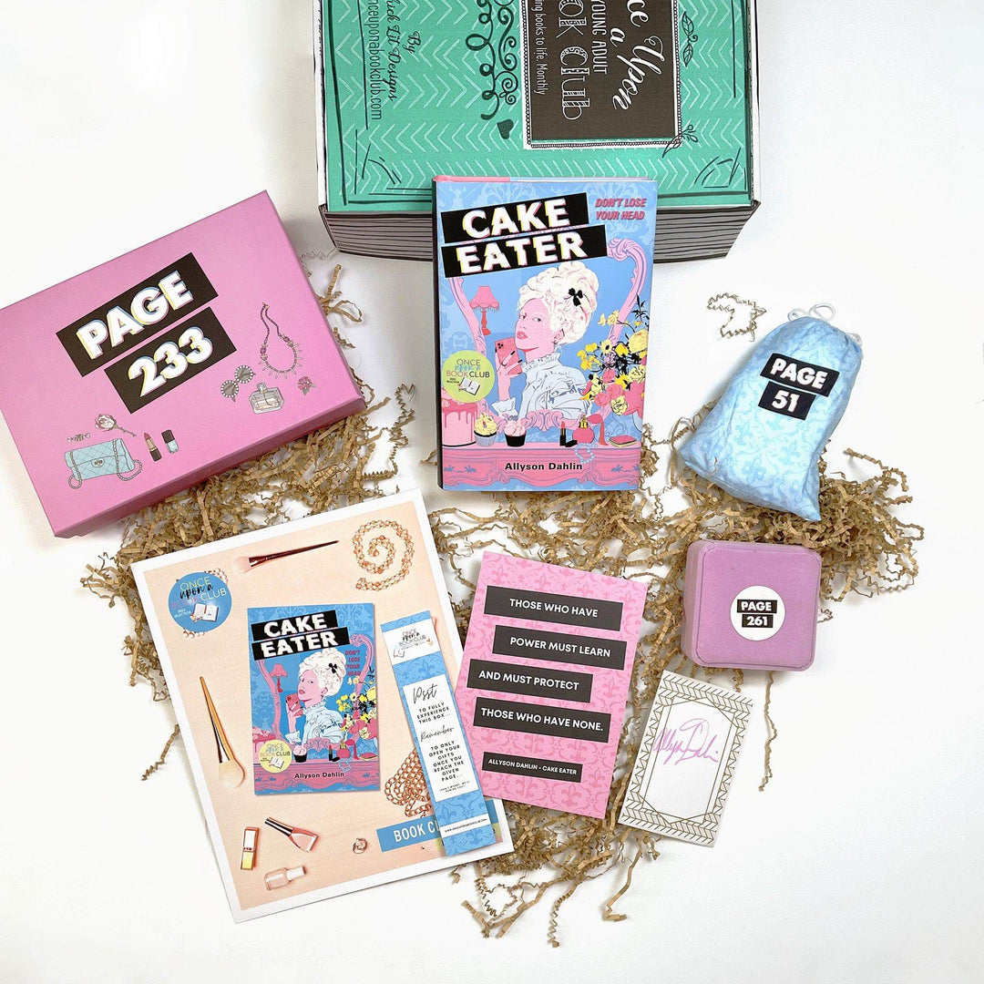 A hardcover edition of Cake Eater lays against a green Once Upon a Book Club box. In front are a pink box, bookclub kit, bookmark, quote card, signature card, pink felt box, blue drawstring bag. All boxes and bags are labeled with page numbers.