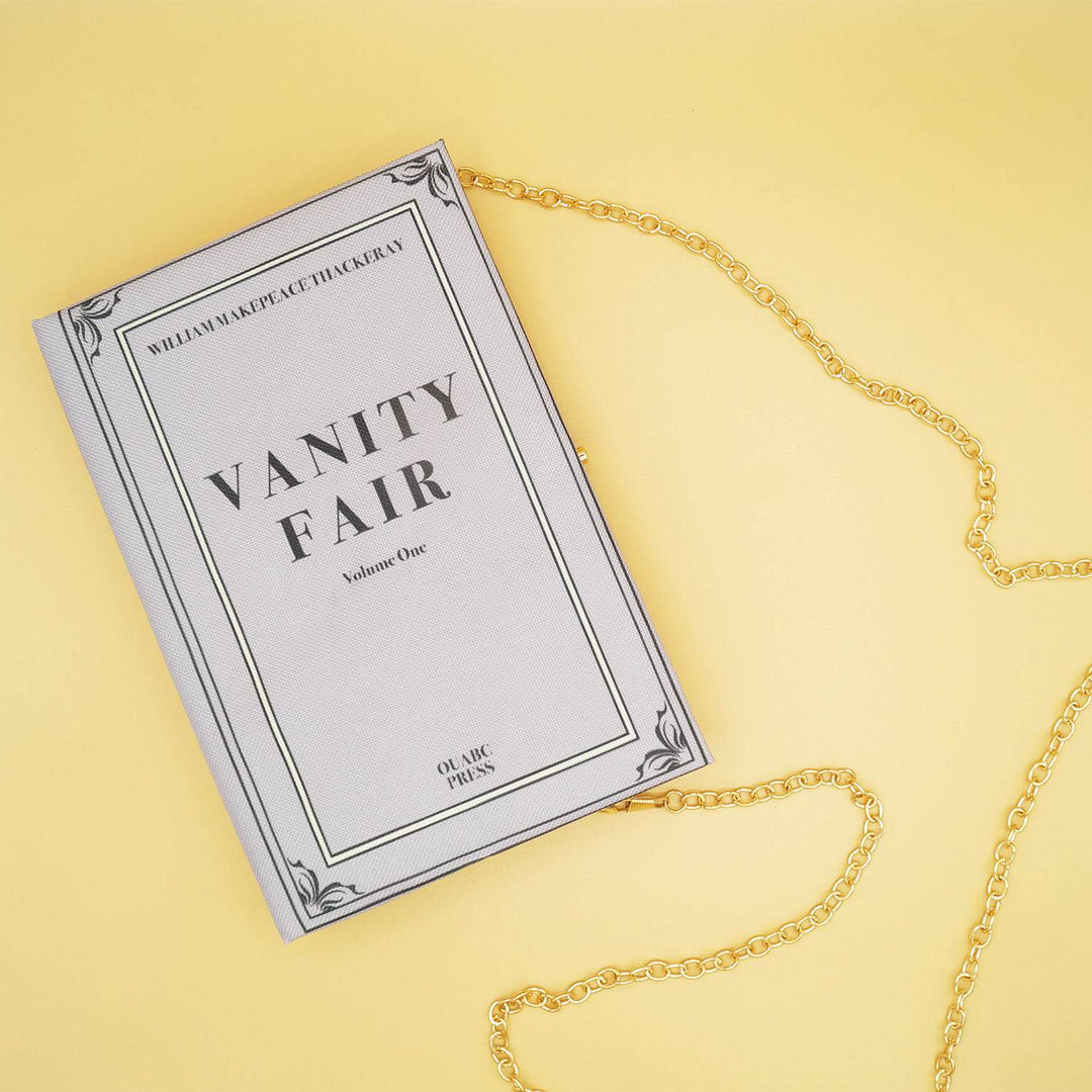 a pale lavender fabric book purse with the words Vanity Fair Volume One in black on the front with a gold metal strap