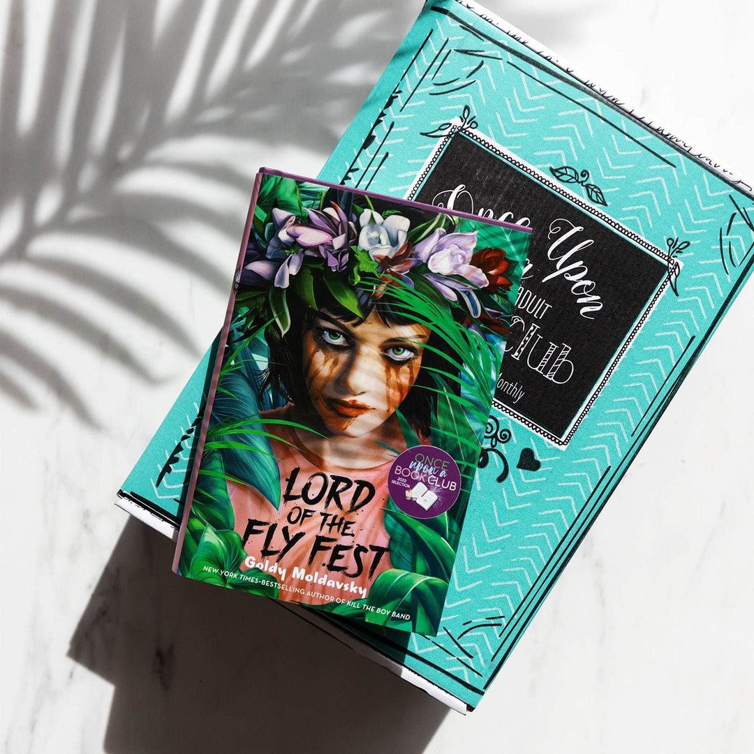 a hardcover edition of Lord of the Fly Fest lays on a green Once Upon a Book Club box with the shadow of a palm frond above it