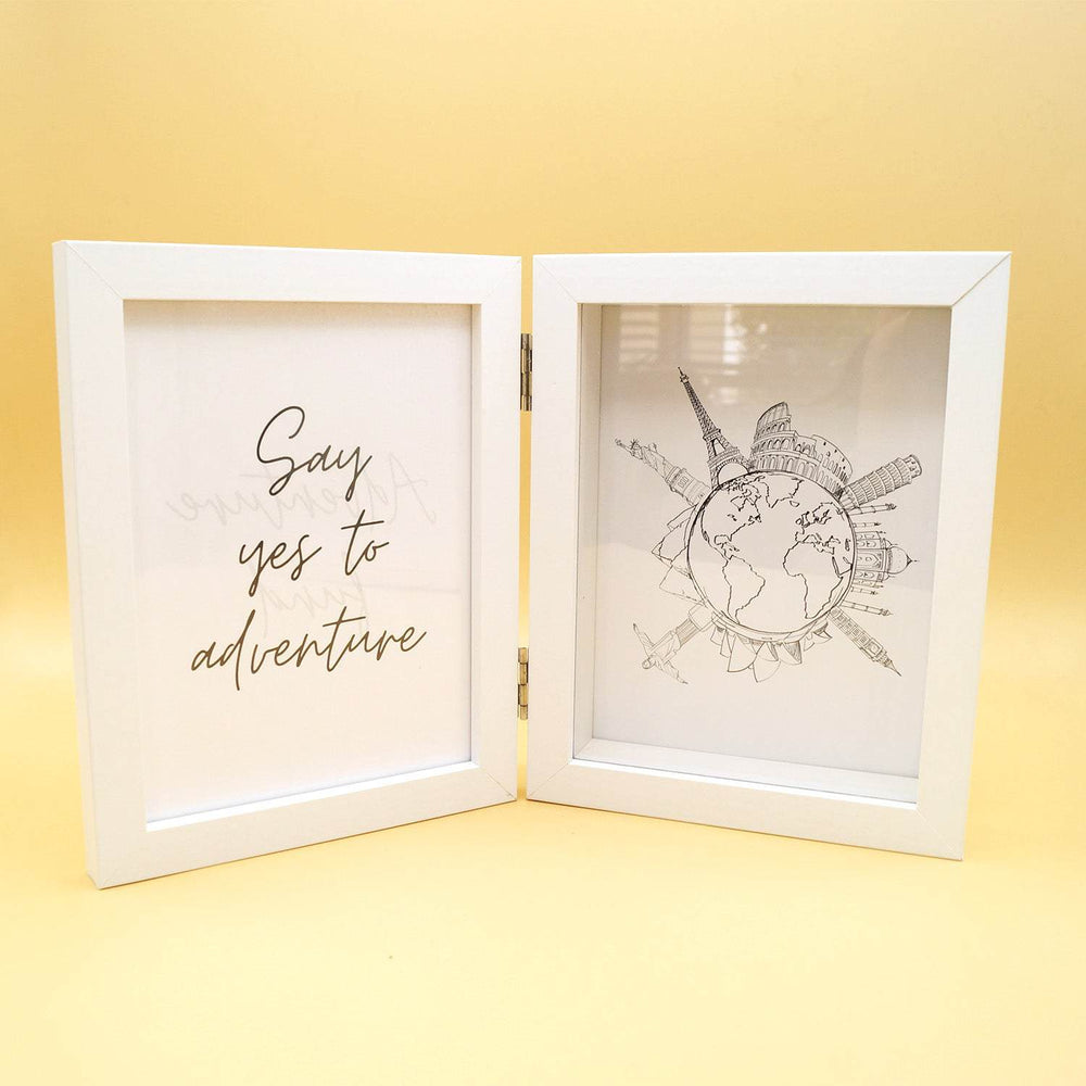a double-sided white frame is open. On the left side is a quote in black "Say yes to adventure" while the right side shows an image of the Earth with monuments sticking out all around it