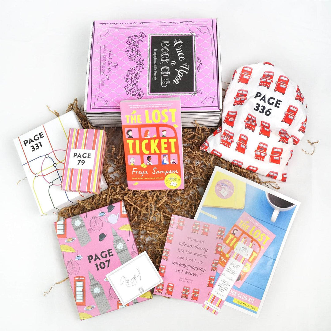 A paperback edition of The Lost Ticket leans against a pink Once Upon a Book Club box. In front are a white box, two pink boxes, signature card, quote card, bookmark, bookclub kit, and white drawstring bag. All bags and boxes are labeled with page numbers.