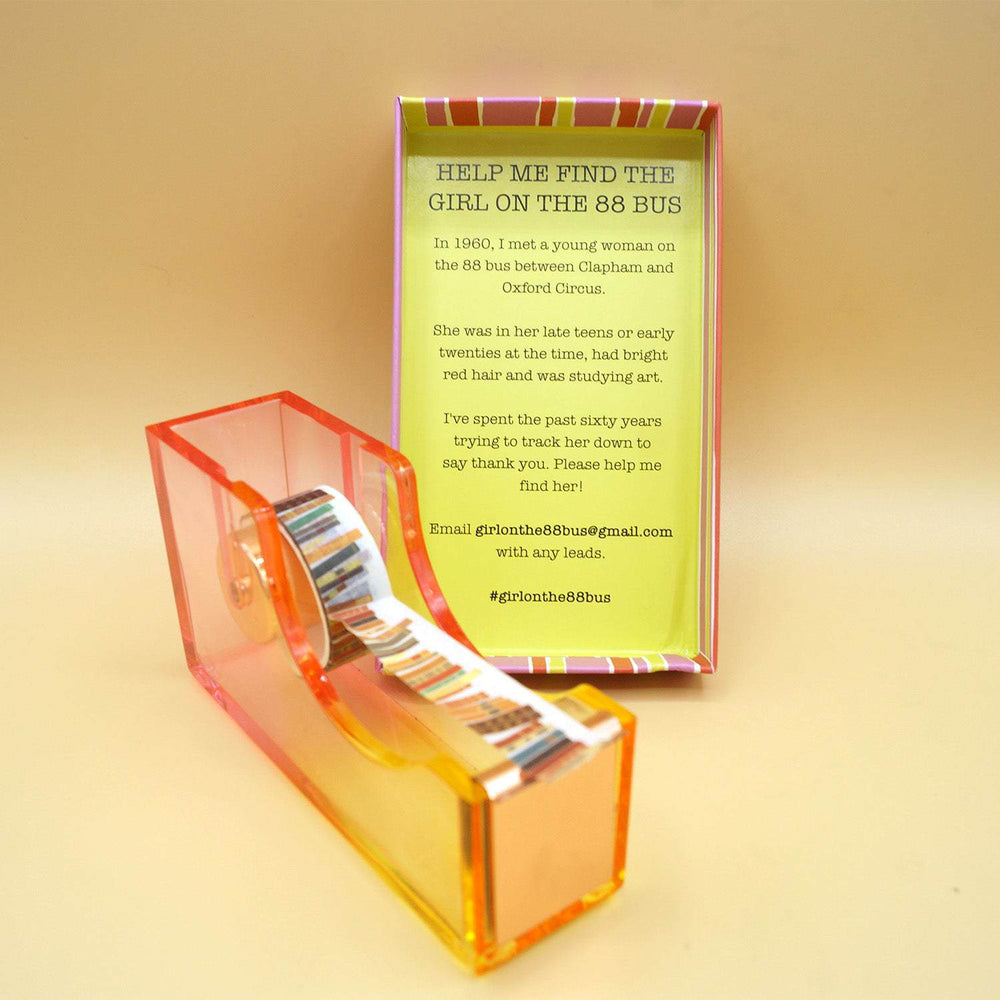 a yellow/pink ombre tape dispenser with book-patterned washi tape next to the lid of a box