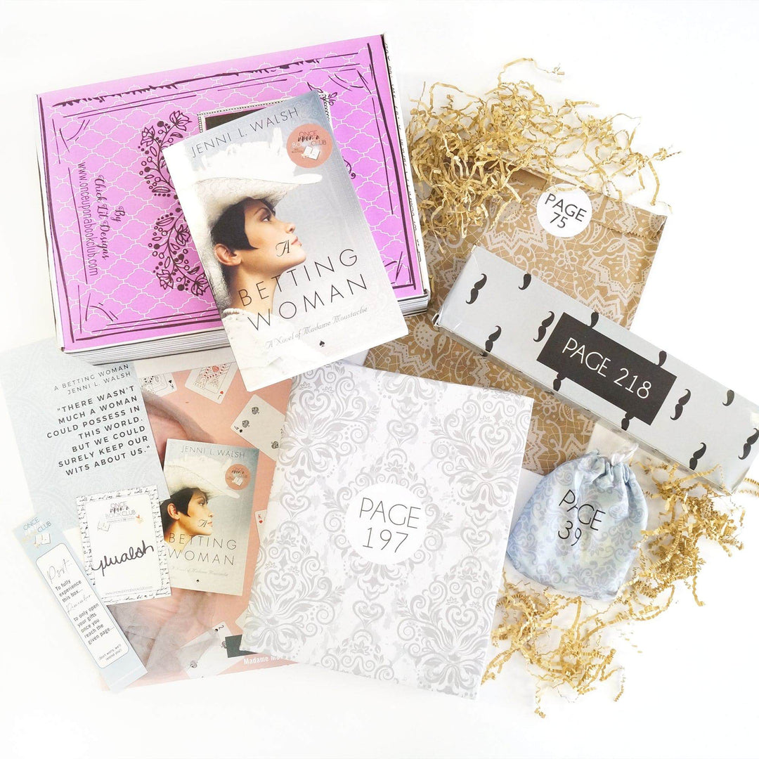 A paperback edition of The Betting Woman on a pink Once Upon a Book Club box. In front of the box (from left to right) are a bookmark, quote card, signature card, bookclub kit, white and gray box, white drawstring bag, brown paper envelope, and white box with mustache pattern. The boxes and bags all have page numbers.