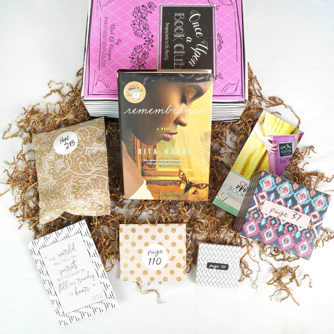 A hardcover edition of Remembrance leans against a pink Once Upon a Book Club box. In front of it are a brown paper bag with white lace pattern, quote card, gold polkadot box, white box, and pink and blue box. The boxes are labeled with page numbers.