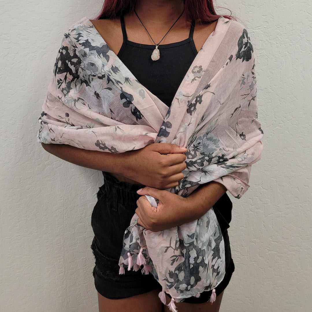 a dark-skinned woman wears a pale pink and black floral scarf around her shoulders