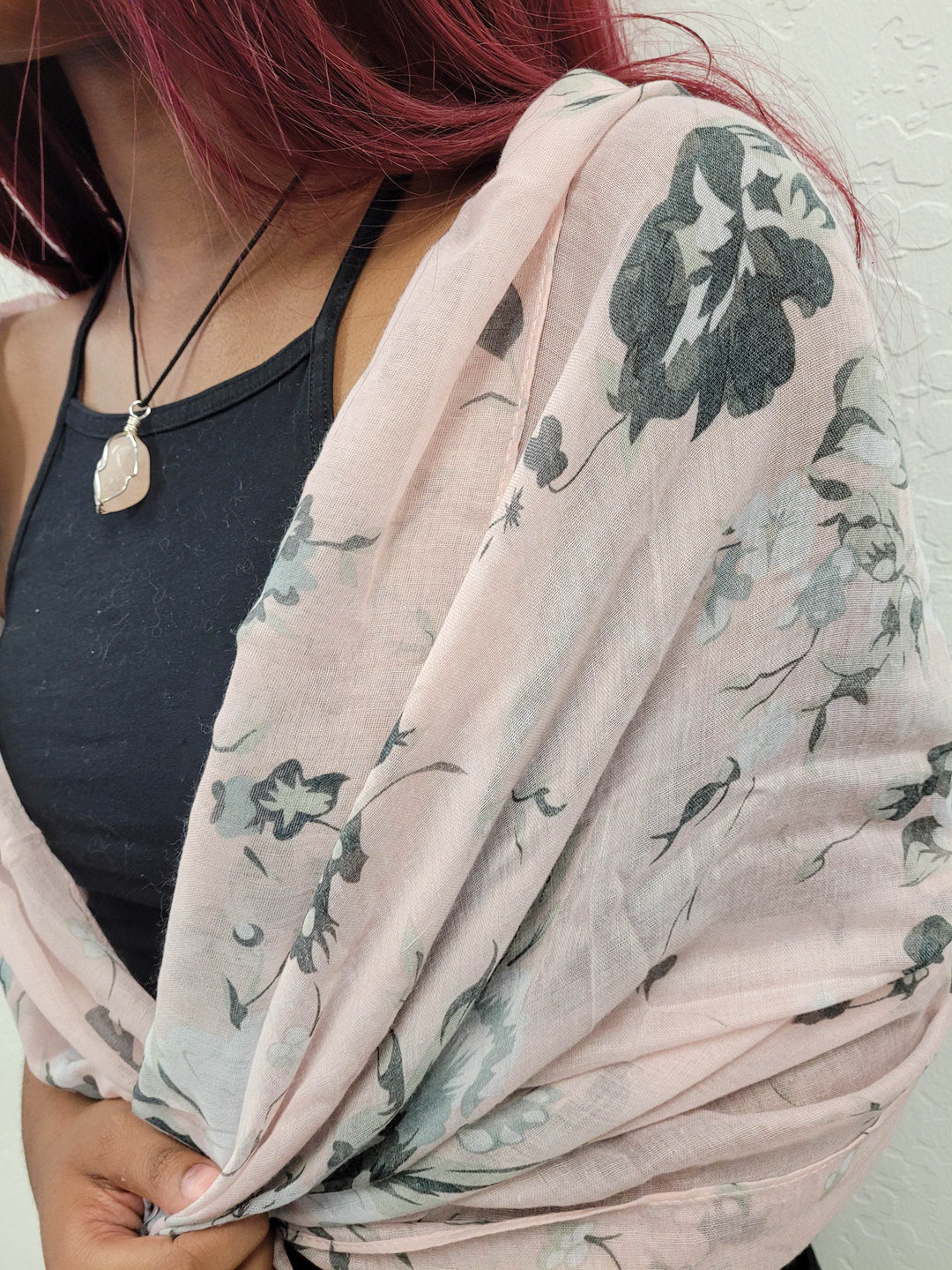 a dark-skinned woman with red hair wears a pale pink pastel scarf with black flowers around her shoulders