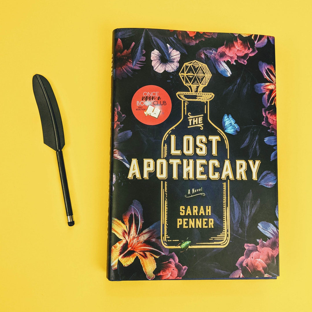 a black quill feather stylus is next to a hardcover edition of The Lost Apothecary