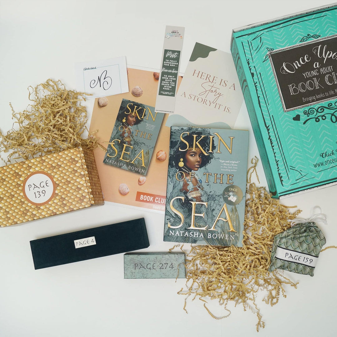 A green Once Upon a Book Club box is on the right side of the image. Next to the box (from left to right) are a yellow box, blue felt necklace box, signature card, bookclub kit, teal box, bookmark, quote card, hardcover edition of Skin of the Sea, and green drawstring bag. The boxes and bags all have page numbers.