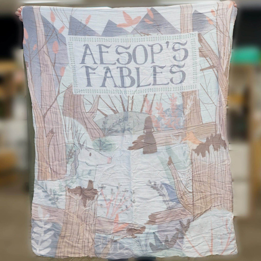 a person holds up a pastel-toned blanket labeled "Aesop's Fables" 