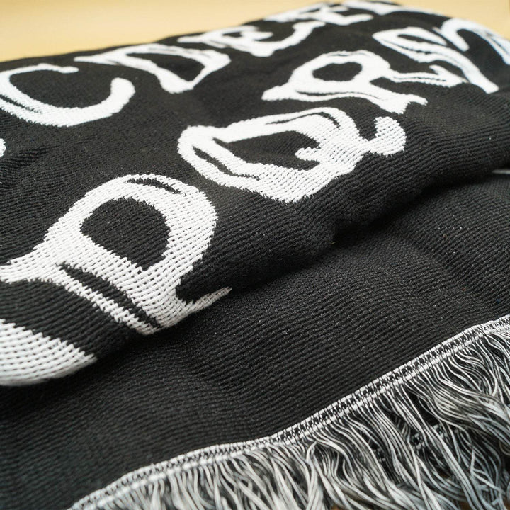 a black woven blanket folded up with black and white tassels