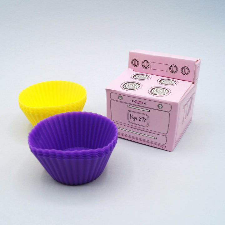 purple and yellow silicone cupcake liners are next to a small pink box shaped like an oven