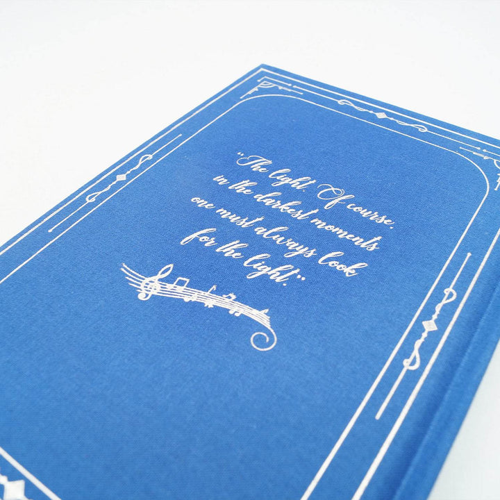 the back hardcase of a special edition of The Lost Melody. The book is blue with a quote in silver: "The light. Of course in the darkest moments one must always look for the light."