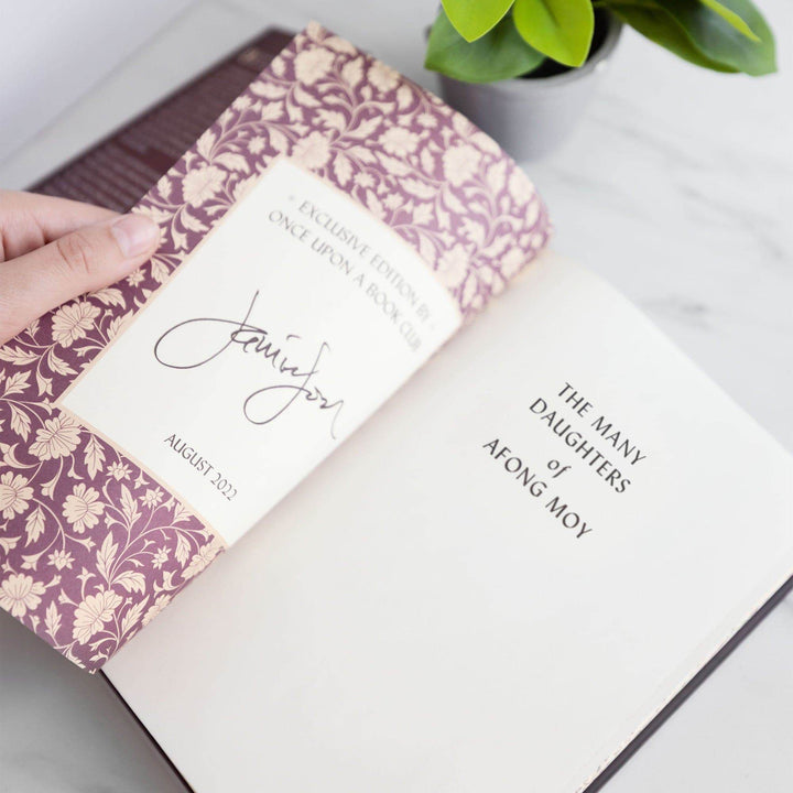 a white hand holds a hardcover special edition of The Many Daughters of Afong Moy open showing the left page has the author's signature on it