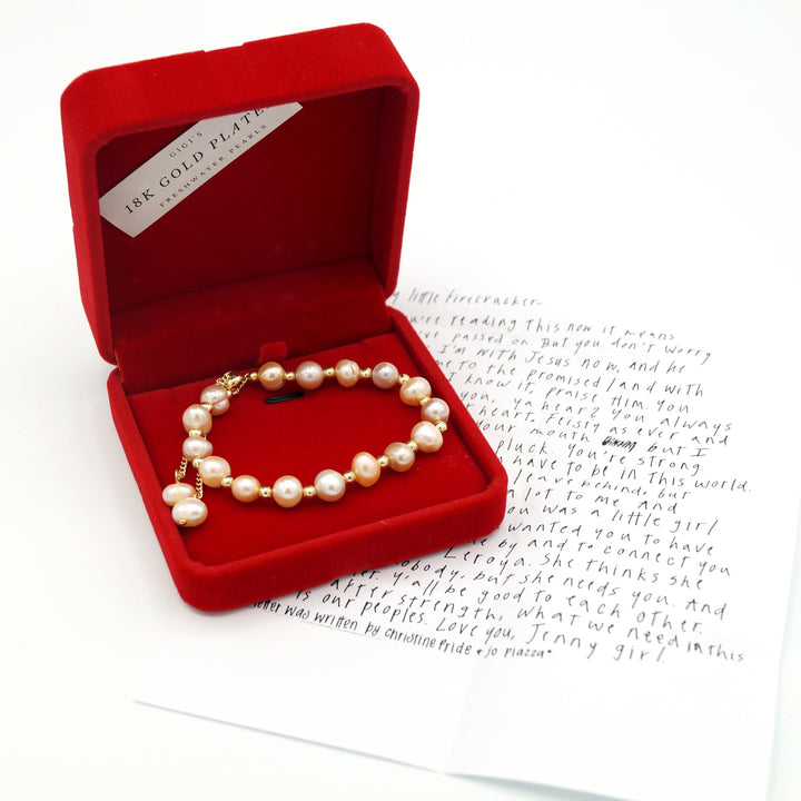 a red felt necklace box is open showing a freshwater pearl & 18k gold bracelet 