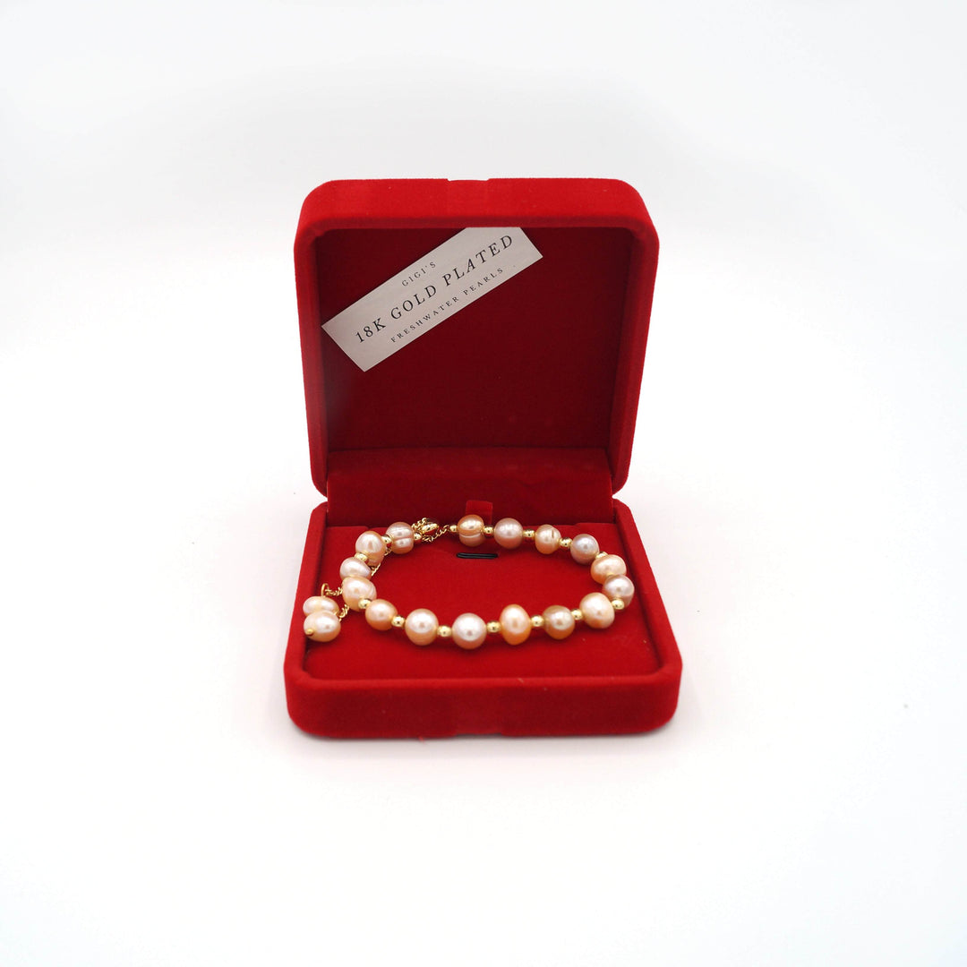 a red felt square box open showing a freshwater pearl & 18k gold bracelet