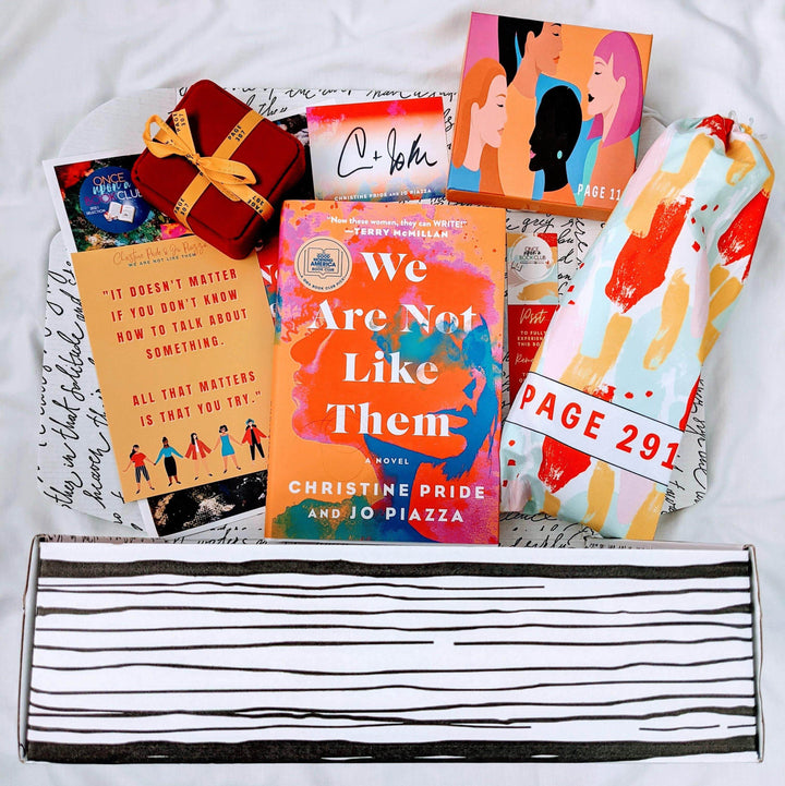 A hardcover edition of We Are Not Like Them is centered in a Once Upon a Book Club box surrounded by a red square box, drawstring bag, orange box with cartoon images of people, and an assortment of paper items. The boxes and bags all have page numbers.