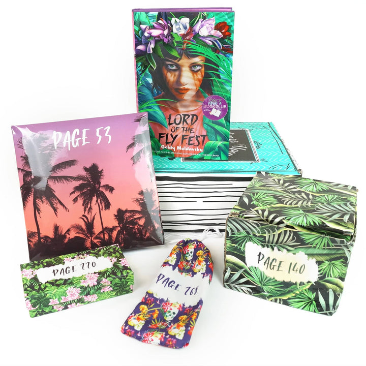 A hardcover edition of Lord of the Fly Fest stands on a green Once Upon a Book Club box. In front of the box are a pink folder, green box, drawstring bag, and green box. All bags and boxes are labeled with page numbers.