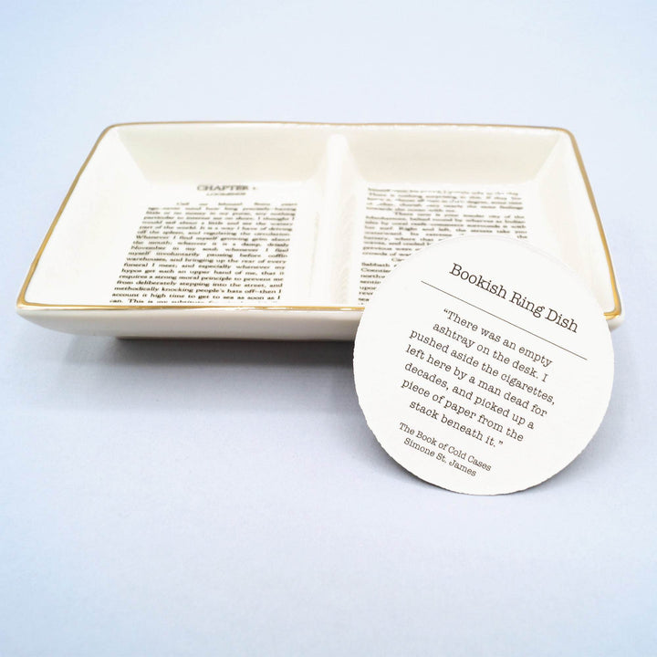 Ceramic ring dish with printed book text and circular card describing its "Bookish Ring Dish" theme.