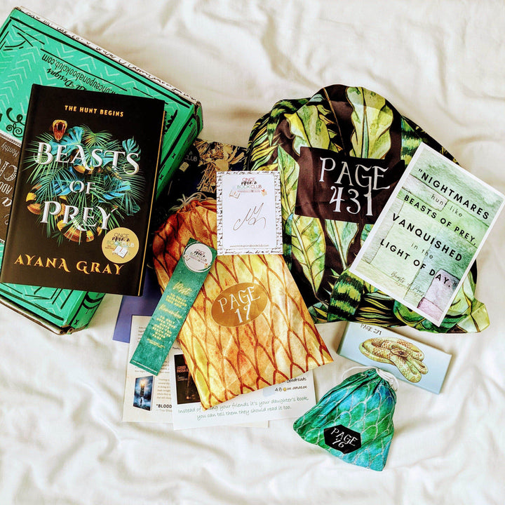 a hardcover edition of Beasts of Prey is on a green Once Upon a Book Club box. Next to the box are a yellow drawstring bag, green and black drawstring bag, small green drawstring bag, rectangular box with a snake on it, and an assortment of paper items. The boxes and bags all have page numbers.
