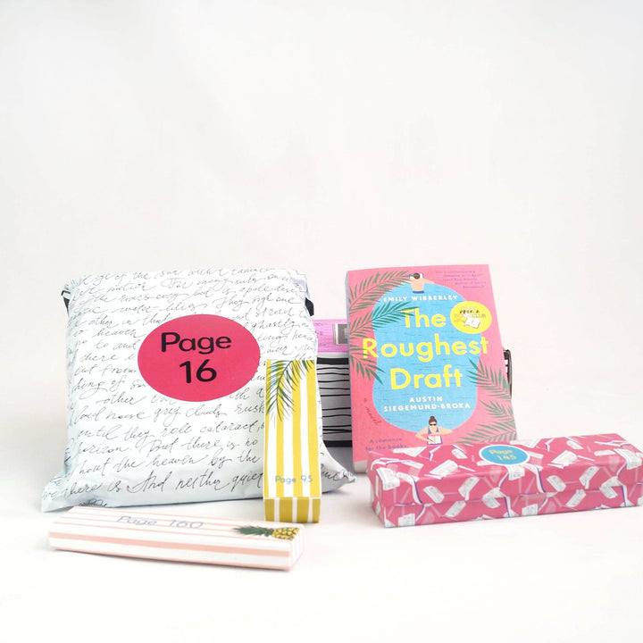 A white polybag and paperback edition of The Roughest Draft are leaning against a pink Once Upon a Book Club box. In front of those are a pink and white box, yellow and white box, and pink box. The boxes and bags all have page numbers.