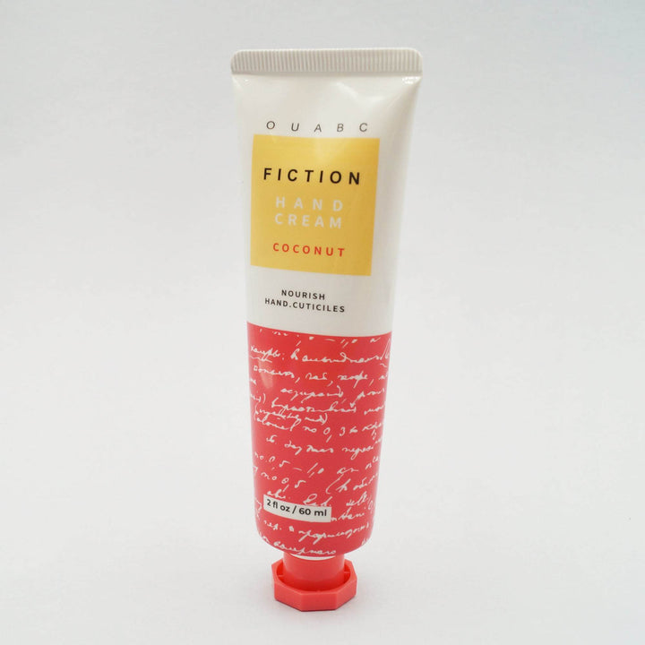 a 2 fl oz red-orange and white tube of "OUABC Fiction Hand Lotion - Coconut" stands against a white background