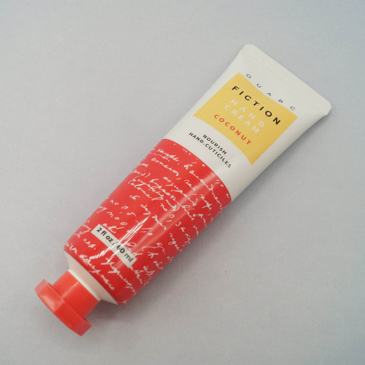 a 2 fl oz red-orange and white tube of "OUABC Fiction Hand Lotion - Coconut" lays on its side