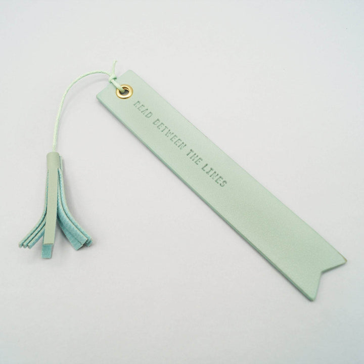 a seafoam green leather bookmark with the quote "Read between the lines"