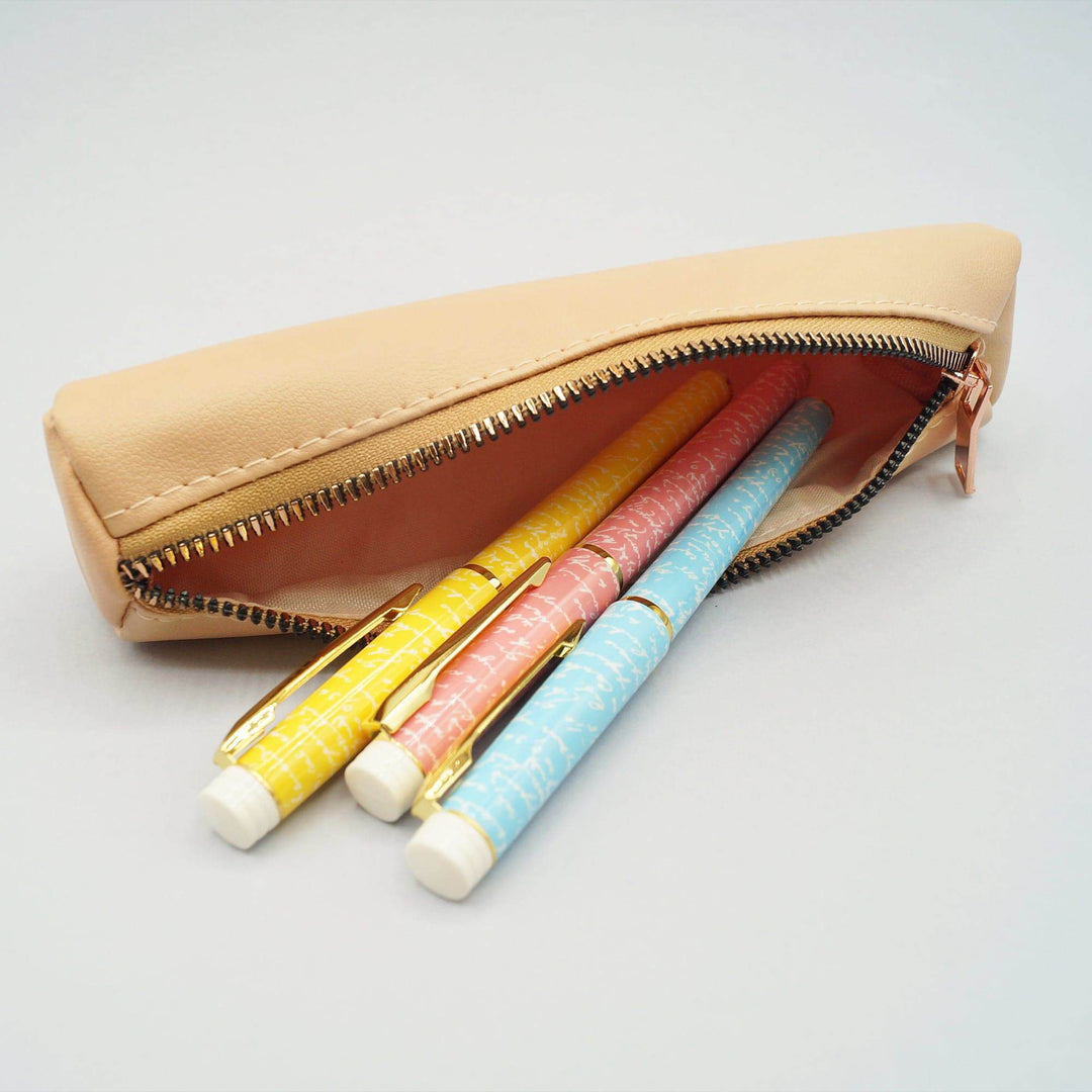 a tan faux leather pencil pouch lays with three pens coming out of it - one yellow, one pink, and one blue