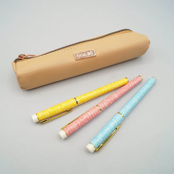 a tan faux leather pencil pouch lays next to three pens - one yellow, one pink, and one blue