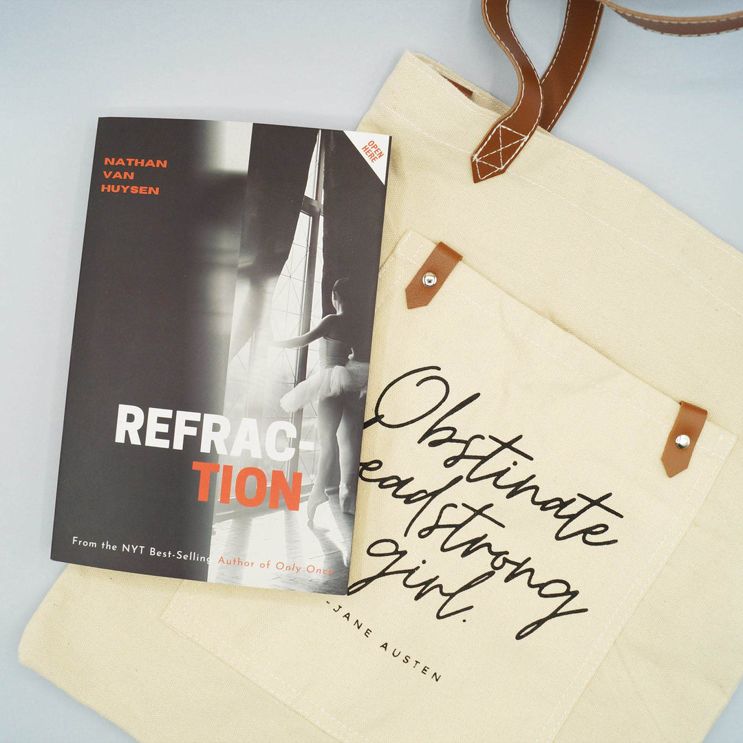 a black and white book titled "Refraction" lays on a beige canvas tote bag printed with the Jane Austen's quote, "Obstinate headstrong girl" 