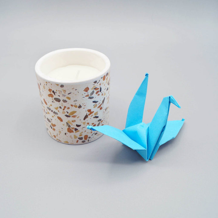 a white speckled candle next to a blue paper crane