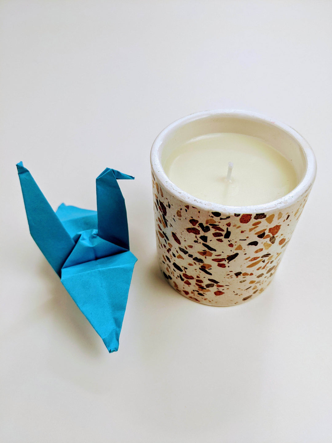 a white speckled candle next to a blue paper crane